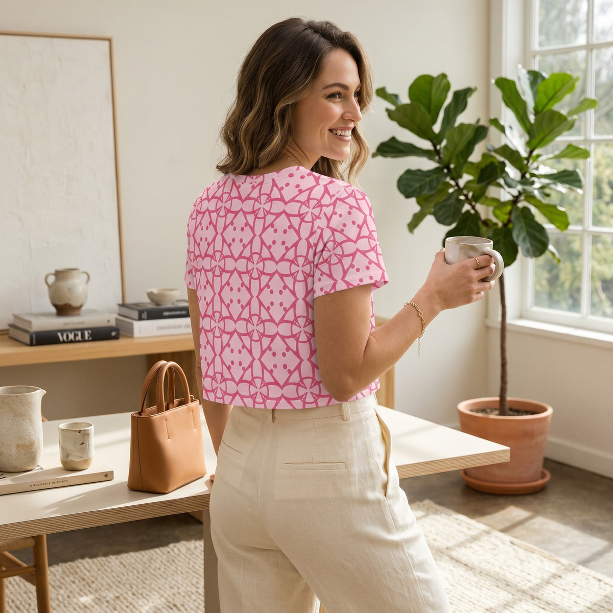 Good Wishes 365 pink crop tee with geometric all-over print worn by a smiling woman in a bright home office setting.