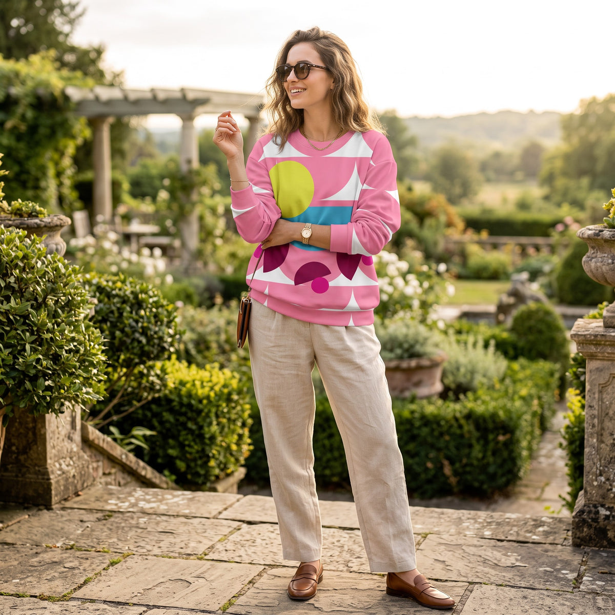 Good Wishes 365 pink geometric mushroom graphic sweatshirt worn by a woman in a garden with beige linen trousers.