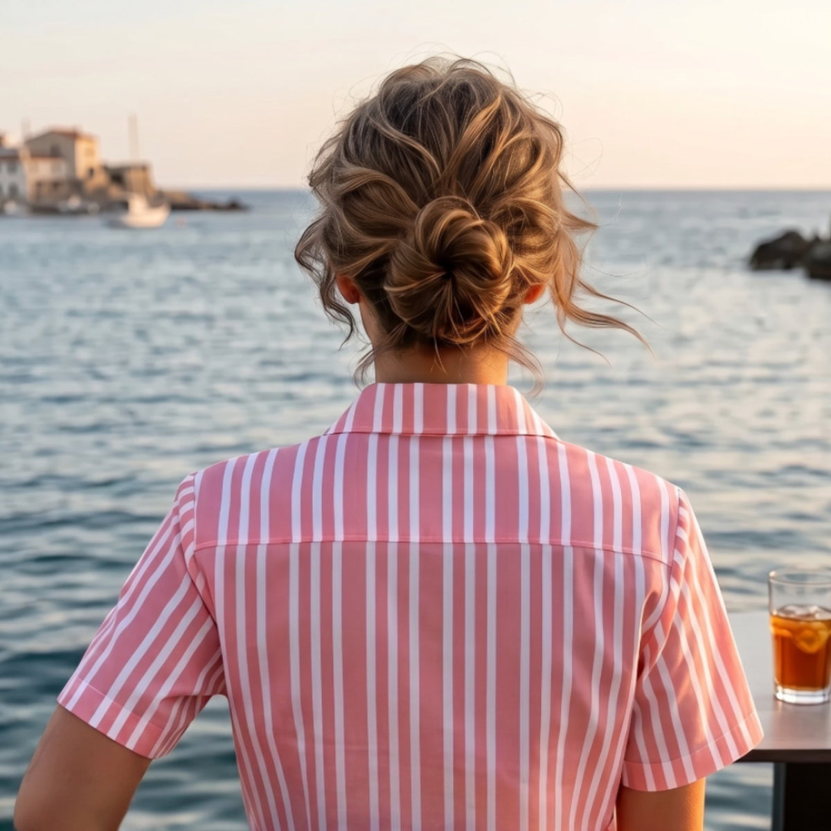 Good Wishes 365 pink and white vertical striped resort shirt with a camp collar worn by a woman overlooking the sea.