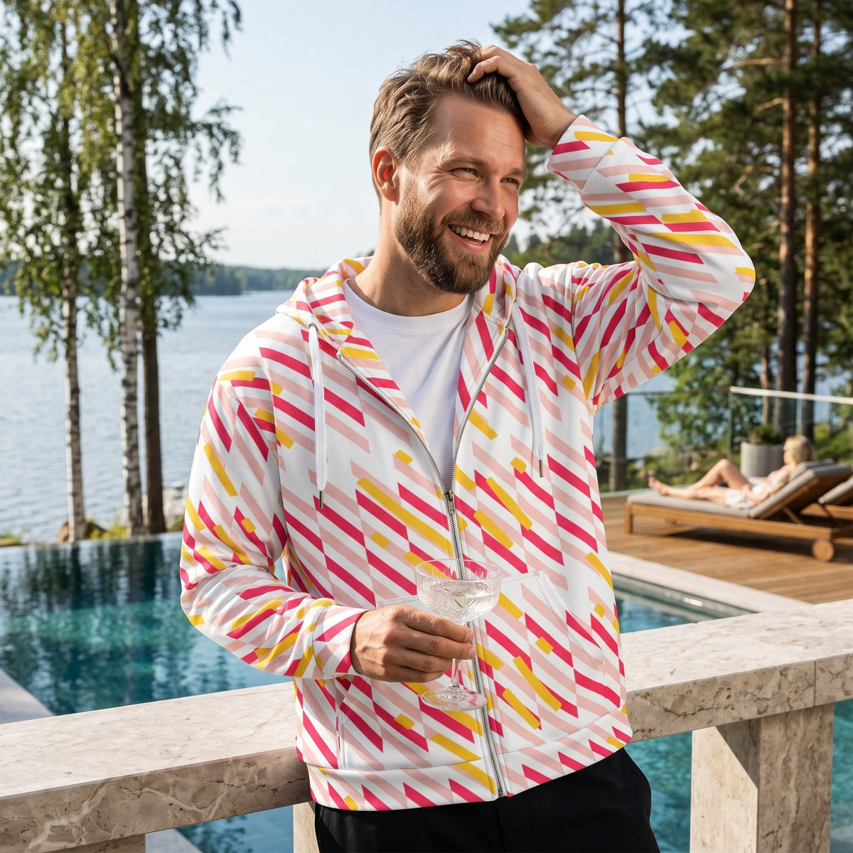 Good Wishes 365 recycled zip hoodie with pink and yellow geometric lines, worn by a man by a sunny outdoor pool.