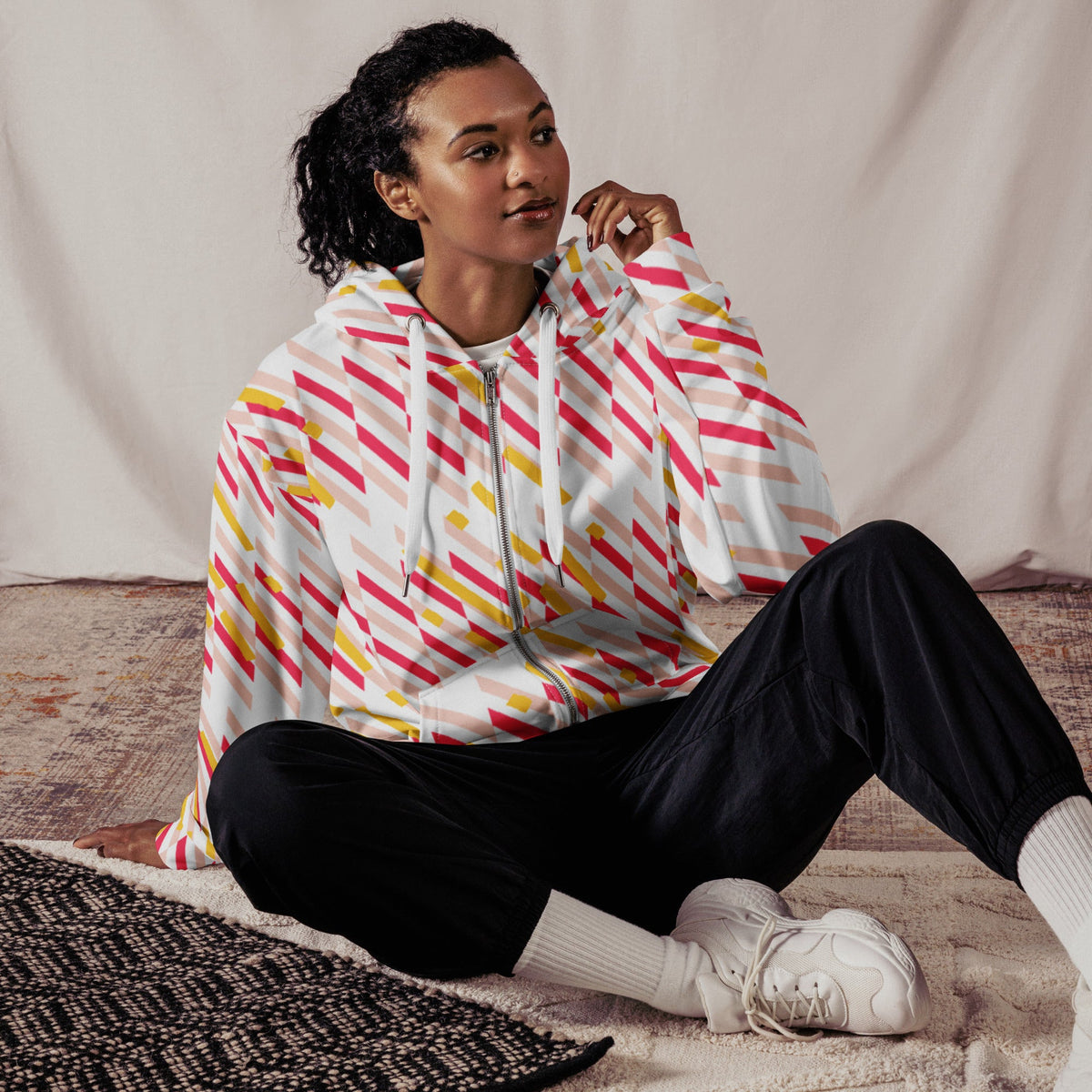 Good Wishes 365 unisex zip hoodie with pink and yellow geometric lines, worn by a model sitting on a textured rug.