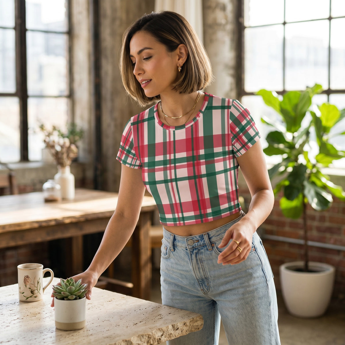 Good Wishes 365 woman wearing a pink and green plaid all-over print crop tee with jeans in a bright loft setting.