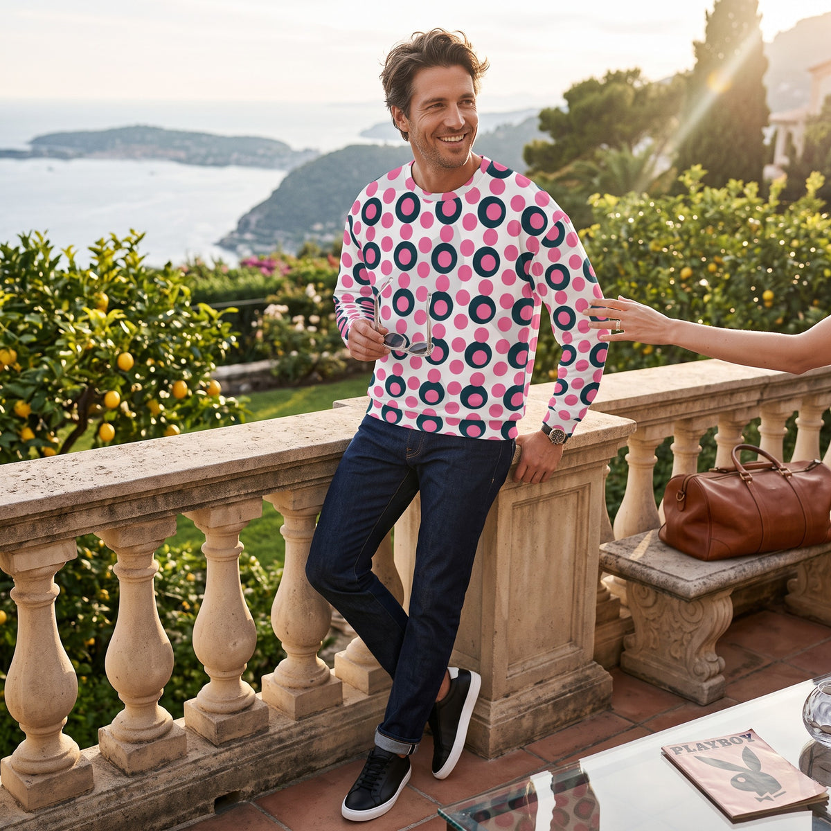 Good Wishes 365 unisex sweatshirt with rose pink and charcoal polka dot print, worn by a man on a sunny terrace.