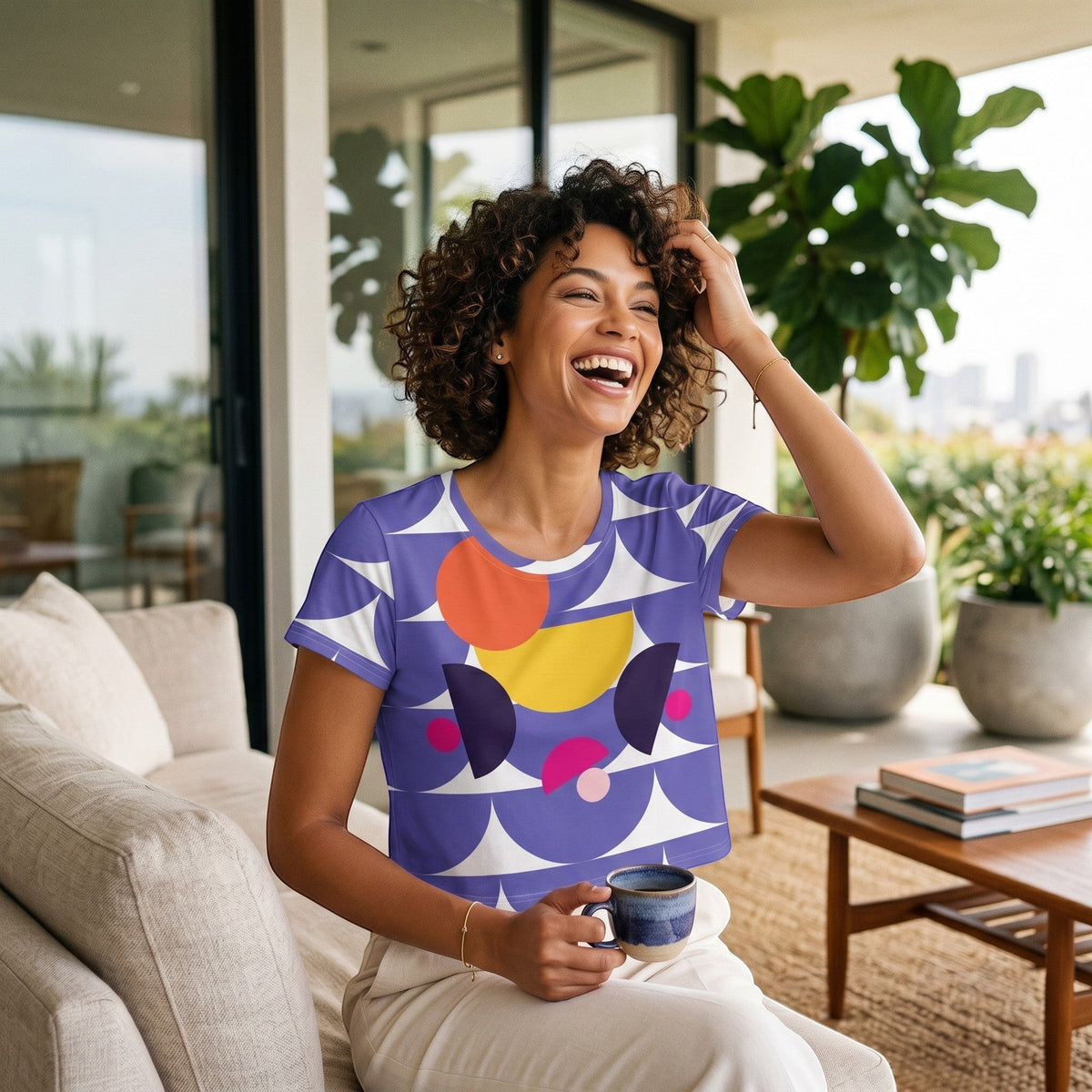 Good Wishes 365 purple crop tee with geometric mushroom graphic worn by a smiling woman in a bright living room.