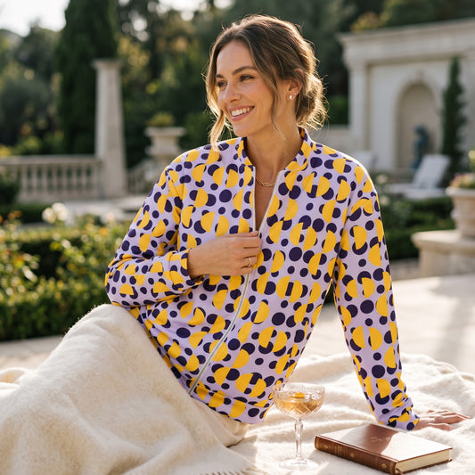 Good Wishes 365 unisex bomber jacket with purple polka dots and yellow semi-circles, worn by a smiling woman outdoors.