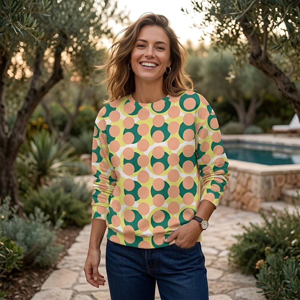 A woman smiling in a Good Wishes 365 pink recycled sweatshirt with a 70s pop art geometric print in a garden setting.
