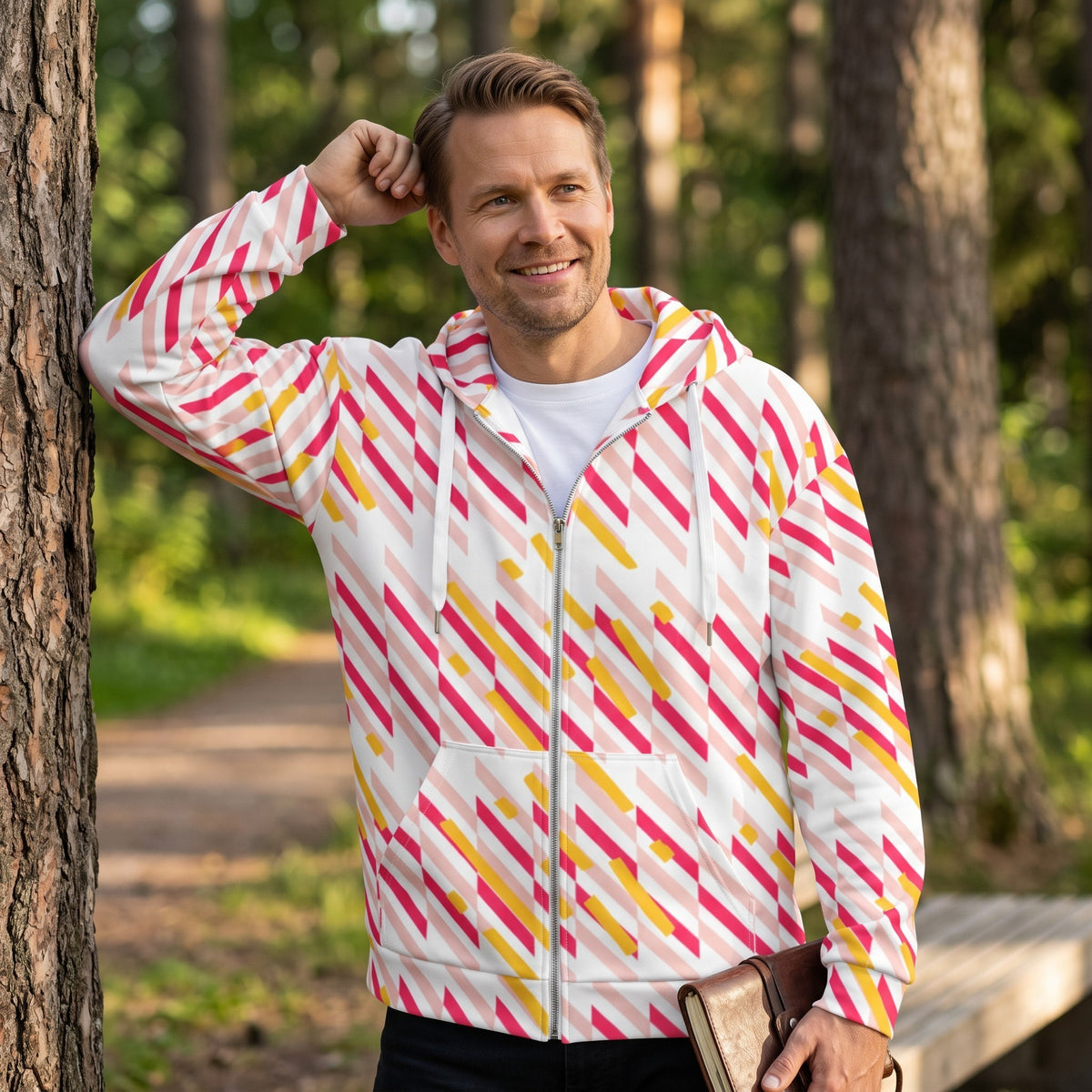 Man wearing a Good Wishes 365 recycled zip hoodie with a pink and yellow geometric line print in a forest setting.