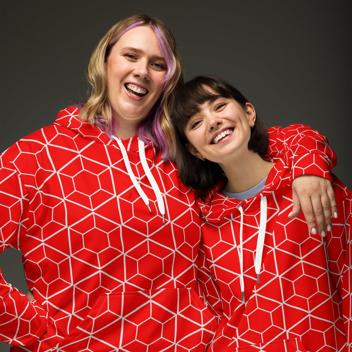 Two smiling women wearing Good Wishes 365 red recycled hoodies with a white geometric hexagon all-over print.