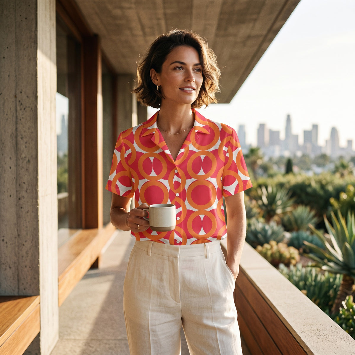 Good Wishes 365 unisex short sleeve button shirt with red and orange geometric pattern worn by a woman on a balcony.