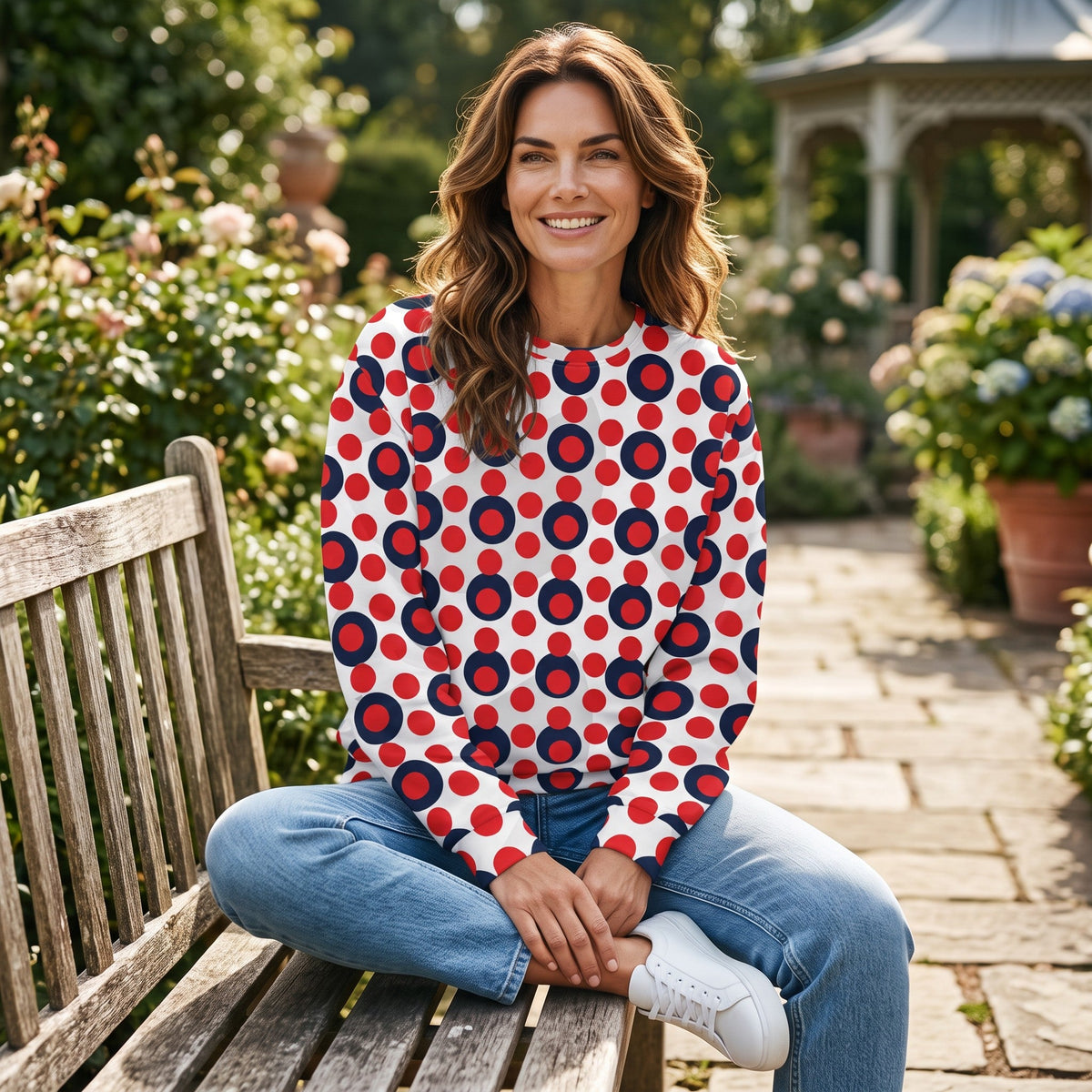 Good Wishes 365 women's recycled sweatshirt with red and navy pop art polka dots, worn by a smiling woman in a garden.