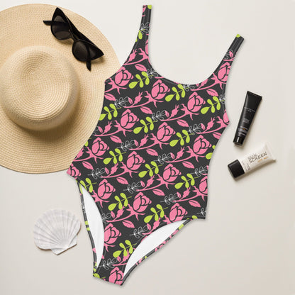 Good Wishes 365 one-piece swimsuit with pink rose floral print on dark background, styled with straw hat and sunscreen