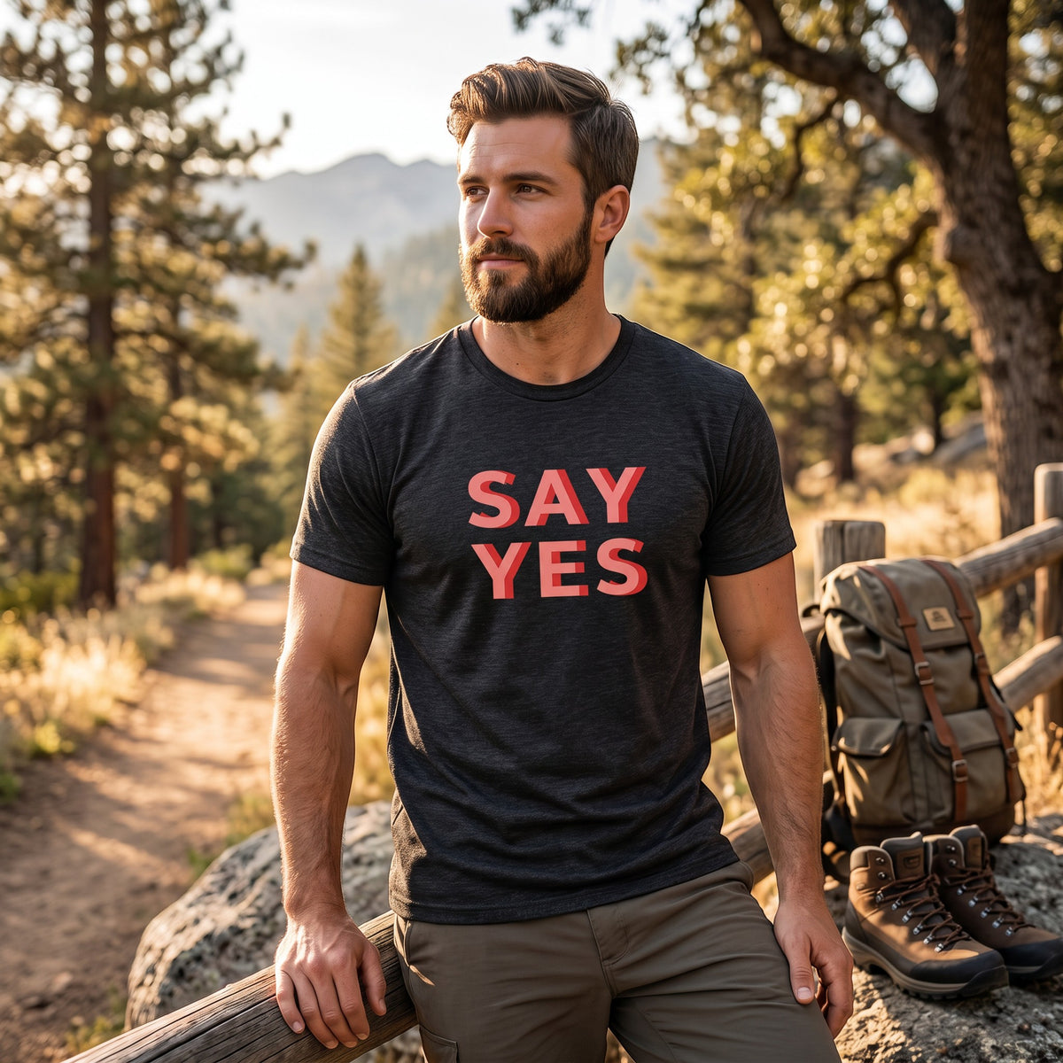 Good Wishes 365 charcoal grey Say Yes graphic t-shirt worn by a bearded man on a sunny forest hiking trail.
