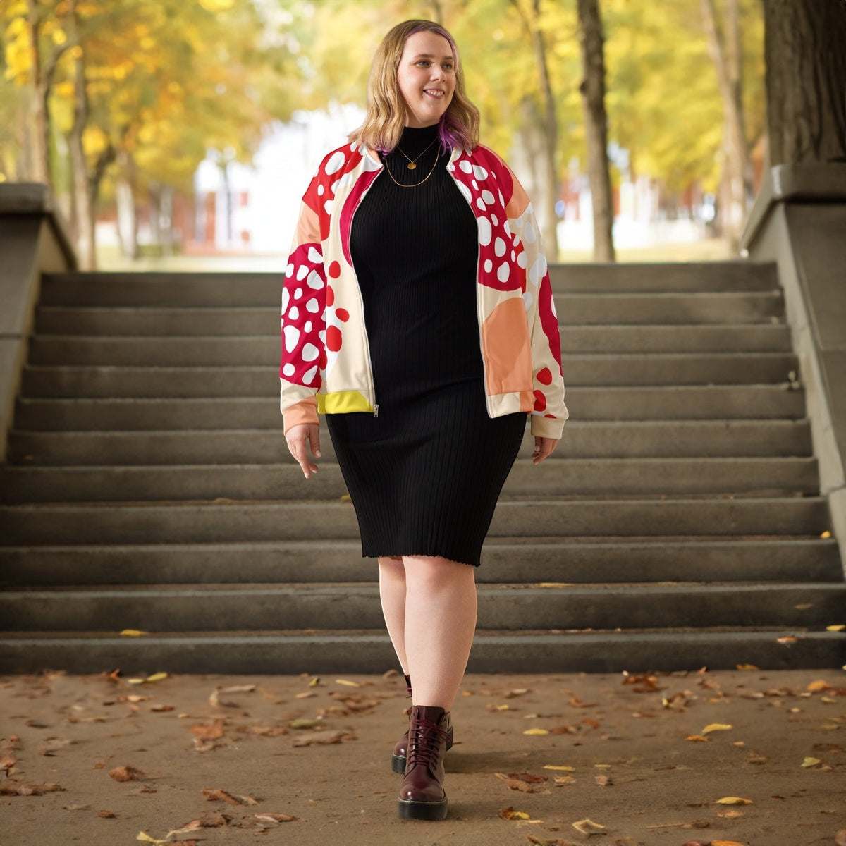 Good Wishes 365 unisex bomber jacket with red strawberry print worn by a woman over a black ribbed dress outdoors.