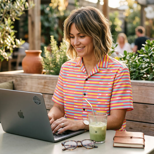 Good Wishes 365 woman wearing a dark pink multicolor striped short sleeve button-up shirt while working on a laptop.