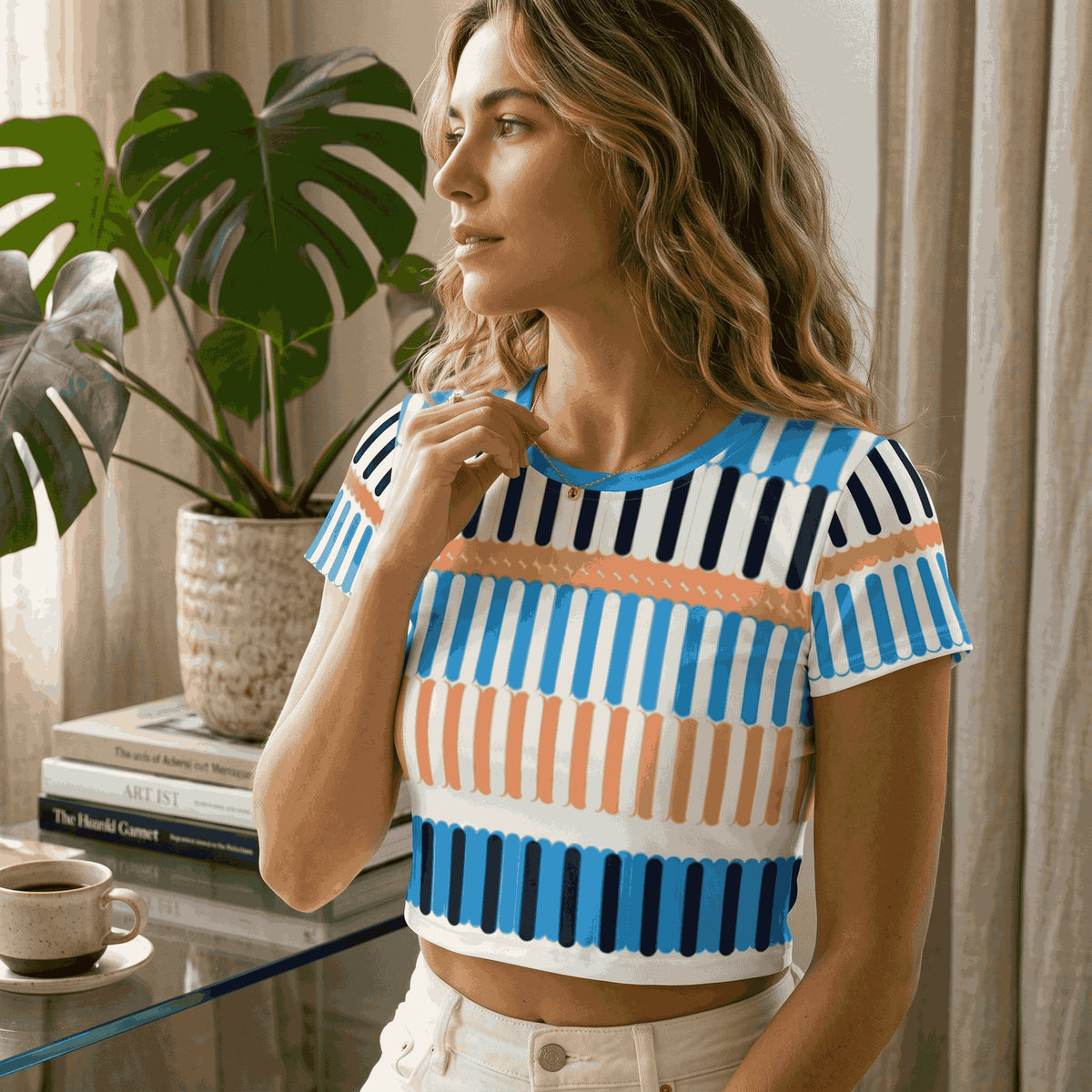 Good Wishes 365 crop tee with blue, navy, and sand vertical stripe print, worn by a woman near a monstera plant.