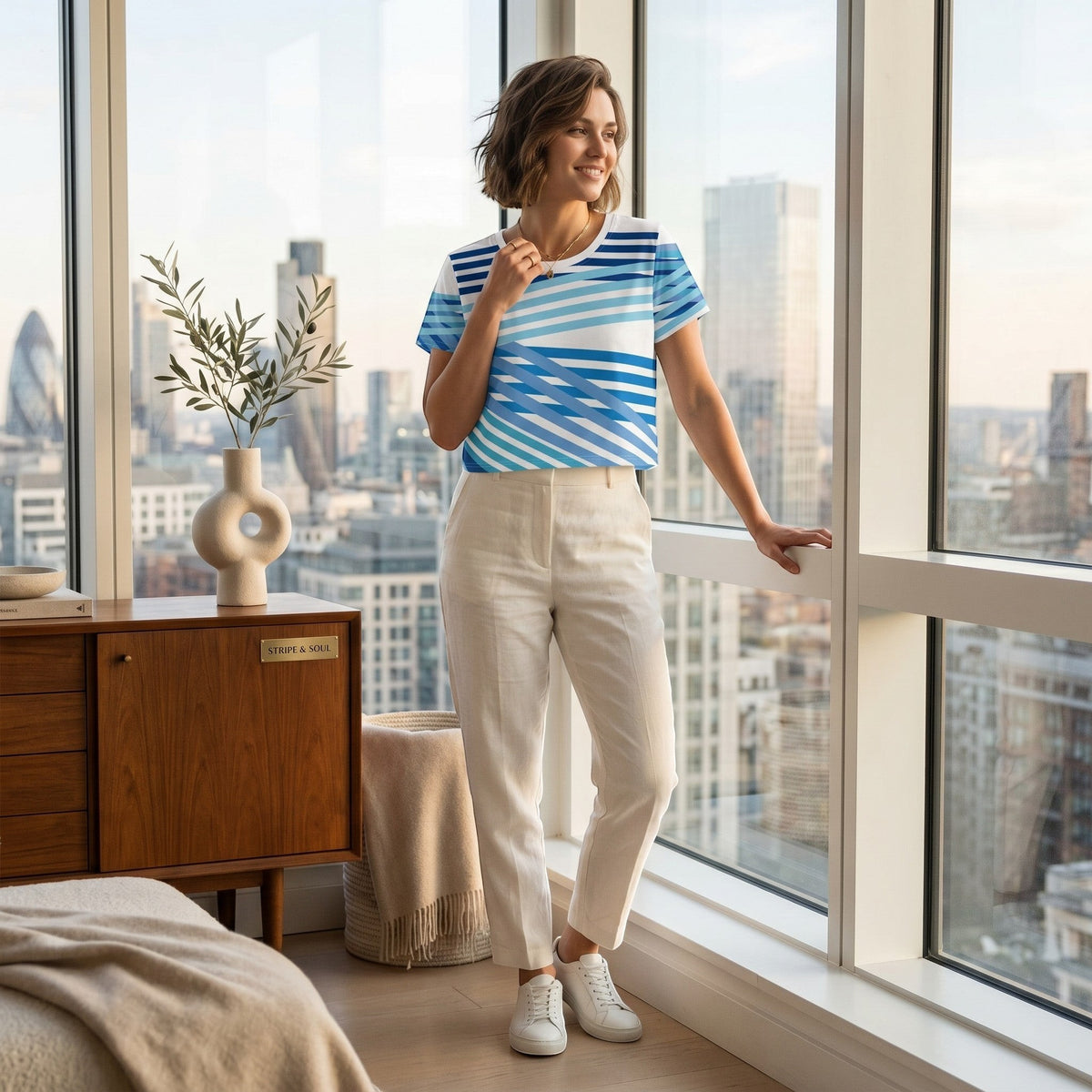 Good Wishes 365 blue and white geometric striped short sleeve crop tee worn by a woman in a bright city apartment.