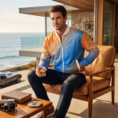 Good Wishes 365 unisex bomber jacket with a blue and orange sunset gradient print, worn by a man on a coastal patio.