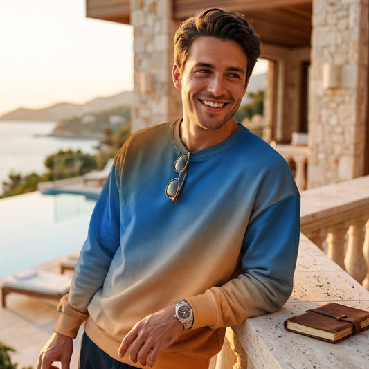 Good Wishes 365 unisex sweatshirt with a blue and orange sunset gradient print, worn by a man on a coastal balcony.