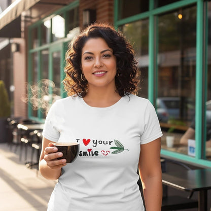 Good Wishes 365 white unisex crewneck t-shirt with I Love Your Smile graphic, worn by a woman holding a coffee cup.