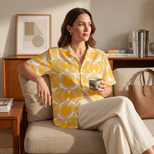 Woman wearing a Good Wishes 365 yellow retro geometric print button-up shirt with a camp collar while sitting on a sofa.