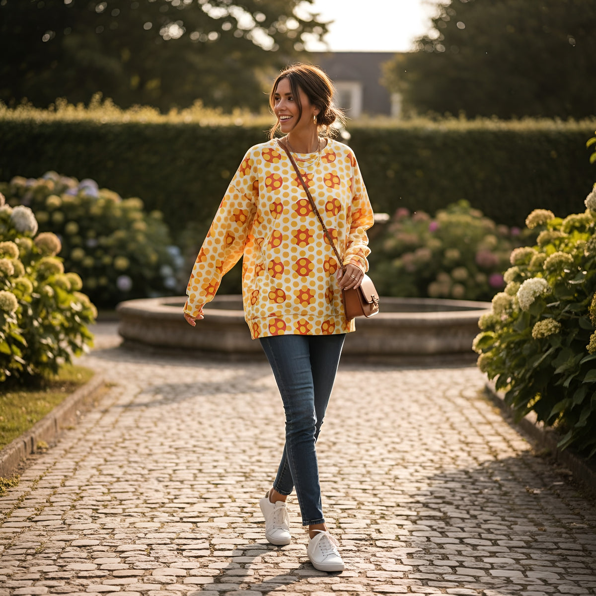 Good Wishes 365 woman wearing a yellow 70s pop art geometric print recycled sweatshirt with jeans in a garden